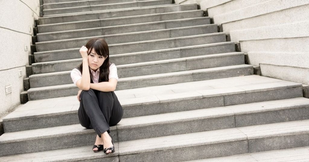 階段に座り込み、不安げな表情を浮かべる女性。引き寄せがうまくいかないと感じる心情を象徴