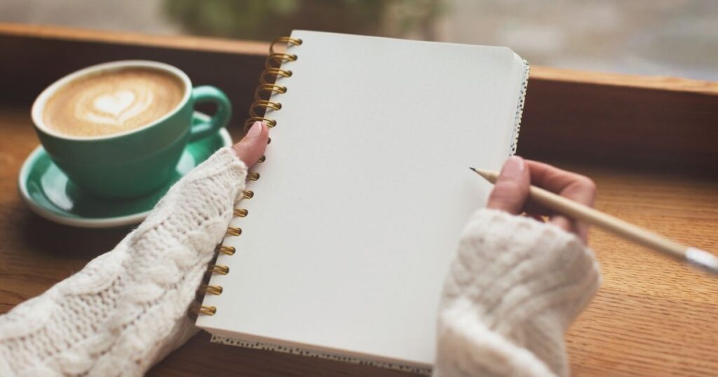 カフェでノートに願いを書く女性の手元。引き寄せの法則ノートとビジョンボードの併用例