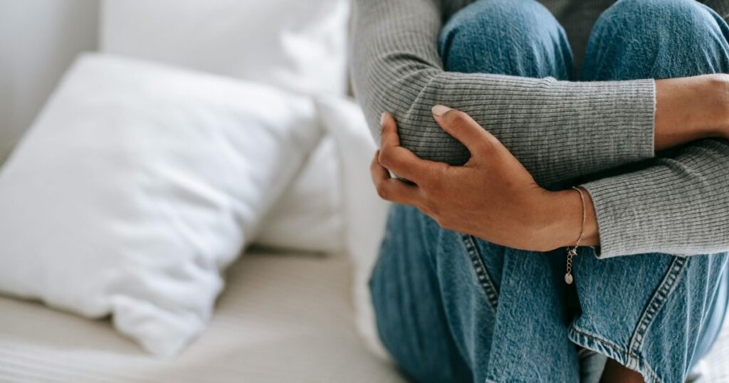 膝を抱えてベッドに座る人物の腕と膝|引き寄せが効かないと感じて疲弊する人の心象を表現