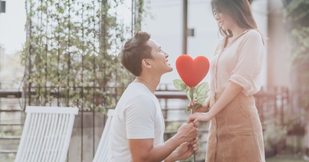 ハート型の花を持ってプロポーズする男性と微笑む女性。理想の恋愛が叶った瞬間の象徴。