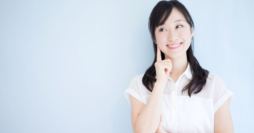指を頬に当てて考える白い服の女性の微笑み